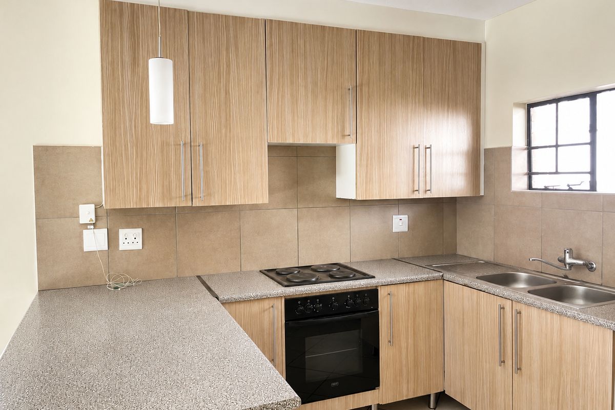 A clean, functional kitchen featuring light wood-grain cabinetry, stone-look countertops, a built-in oven with electric hob, and a double stainless steel sink.