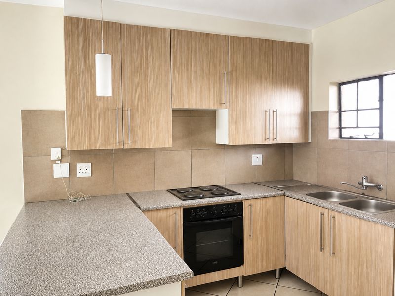 A clean, functional kitchen featuring light wood-grain cabinetry, stone-look countertops, a built-in oven with electric hob, and a double stainless steel sink.
