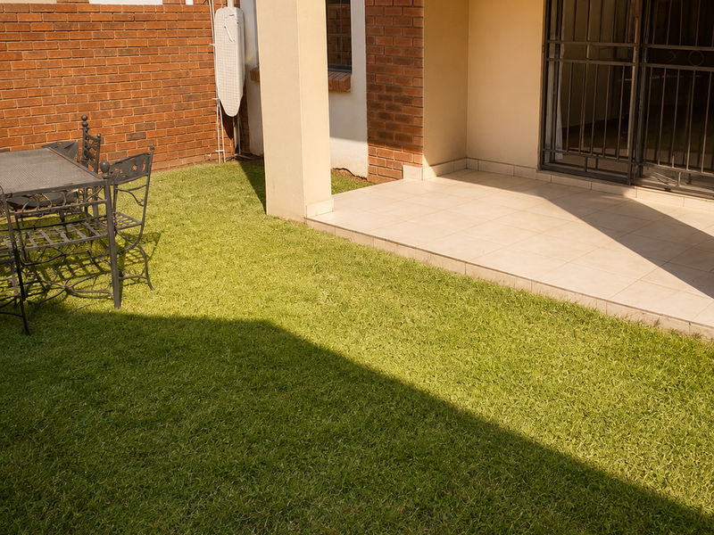 A private rear garden featuring a tiled patio area, brick boundary wall, and secure sliding door access to the apartment interior.