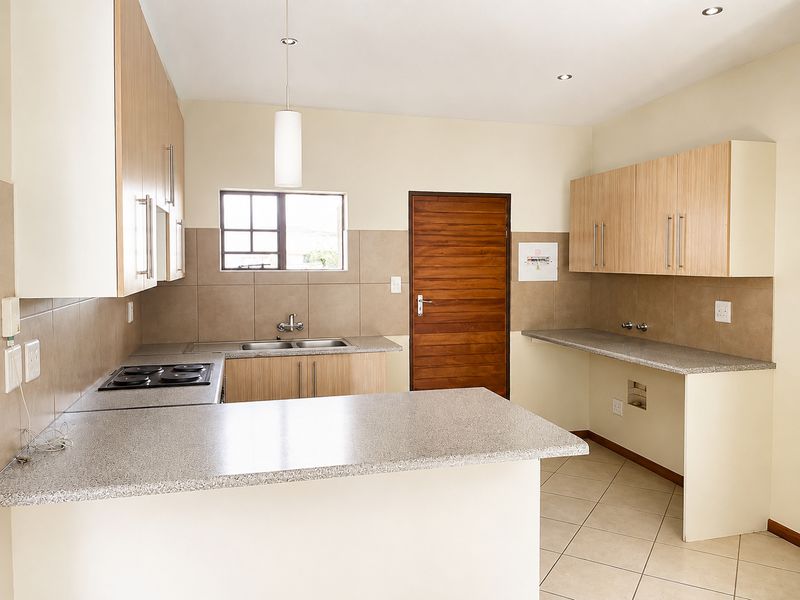 A clean, functional kitchen featuring light wood cabinetry, granite countertops, a built-in electric hob, and tiled flooring with dedicated plumbing for appliances.