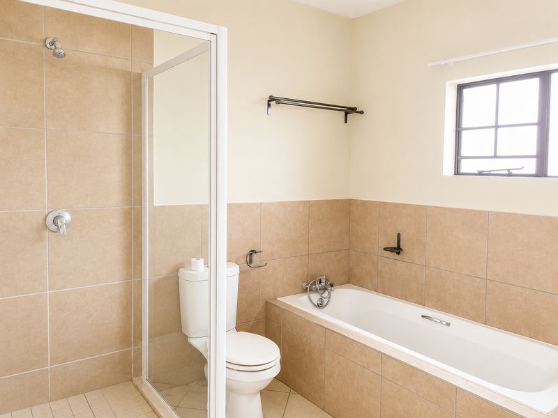 A clean, functional bathroom featuring a separate shower enclosure, a bathtub, and neutral wall tiling.