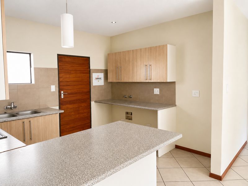 A clean, functional kitchen featuring laminate cabinetry, granite-look countertops, tiled splashbacks, and dedicated plumbing connections for appliances.