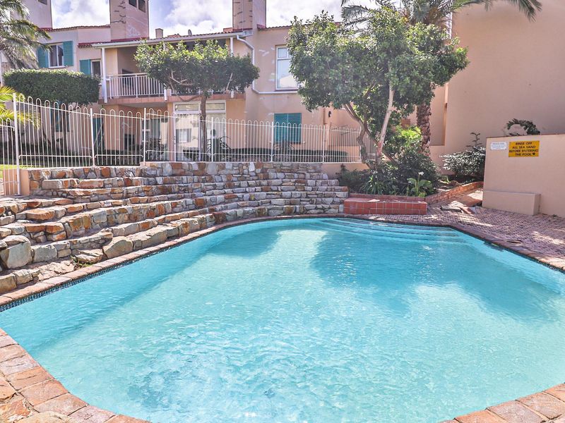 Communal swimming pool area featuring a stone retaining wall, brick paving, and established landscaping within a townhouse complex.