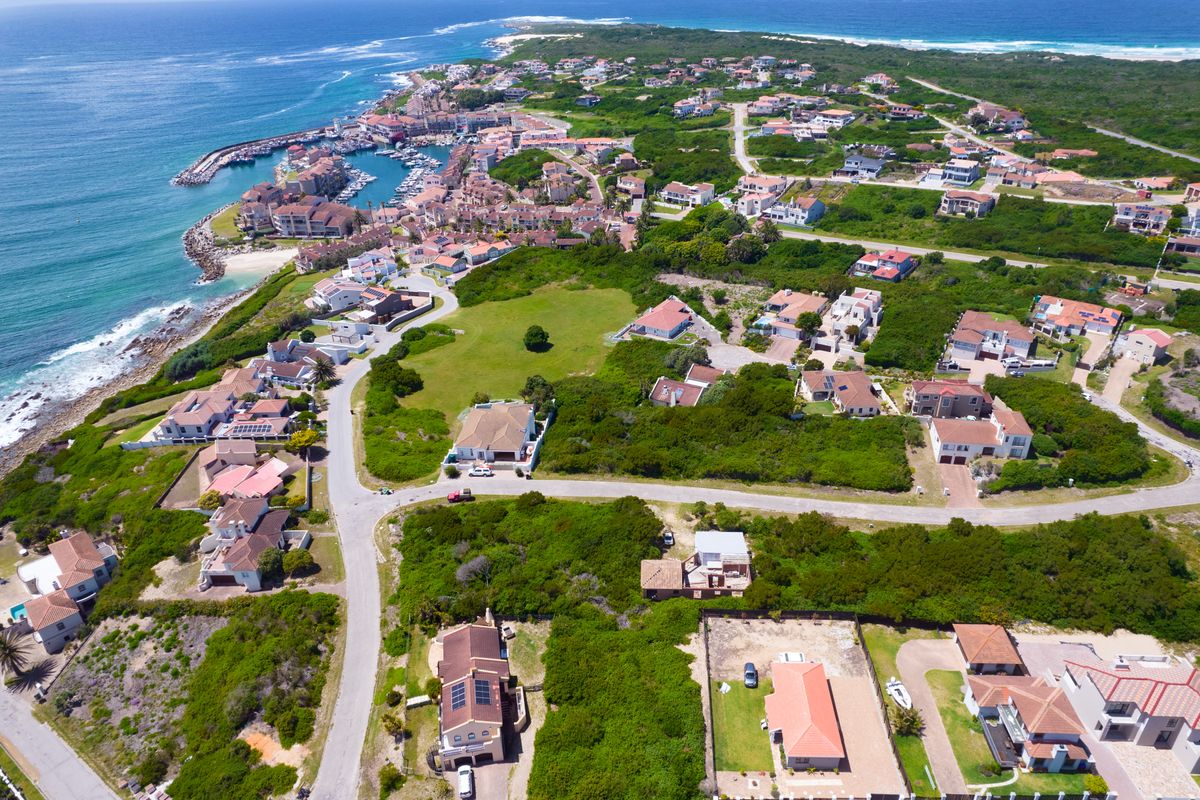 An aerial view of a coastal residential estate featuring paved roads, established vegetation, and proximity to the marina and ocean.