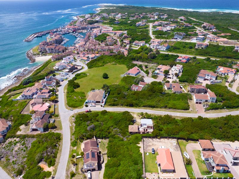 An aerial view of a coastal residential estate featuring paved roads, established vegetation, and proximity to the marina and ocean.