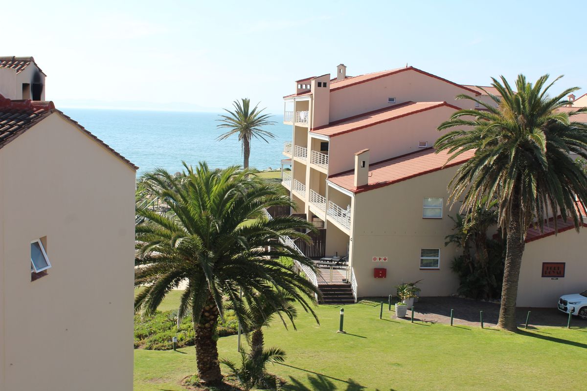 An elevated view of the townhouse complex exterior, featuring terracotta roof tiles, private balconies, and well-maintained garden grounds overlooking the ocean.