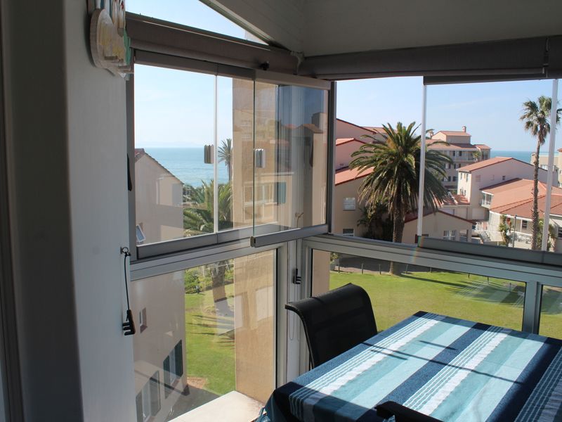 Enclosed balcony featuring frameless glass sliding panels, offering expansive views of the surrounding estate and ocean.