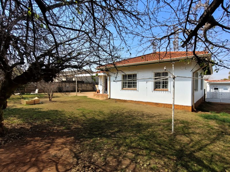 Rear view of the house featuring a garden, covered patio area, and traditional terracotta roof tiles with security bars on windows.