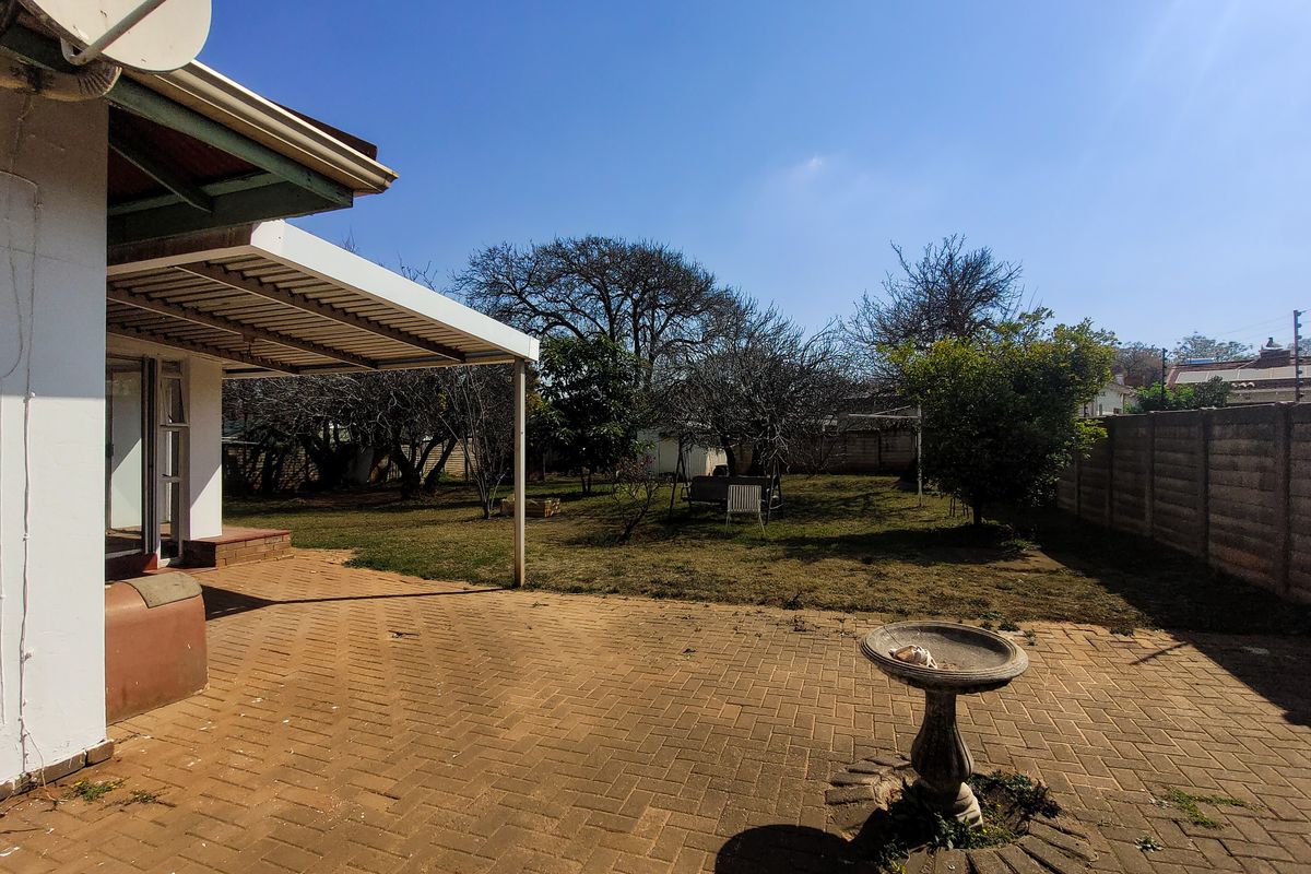 A rear garden featuring a paved patio area, covered veranda, and perimeter boundary walling.