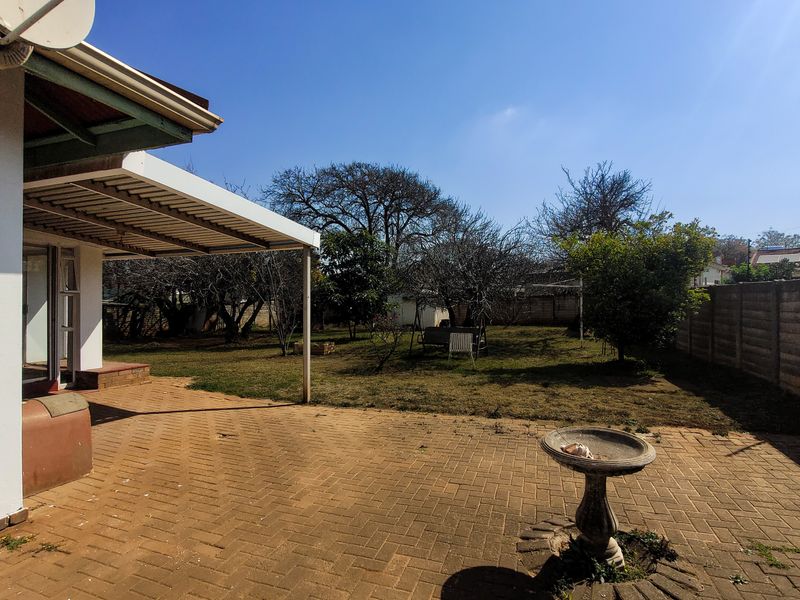 A rear garden featuring a paved patio area, covered veranda, and perimeter boundary walling.