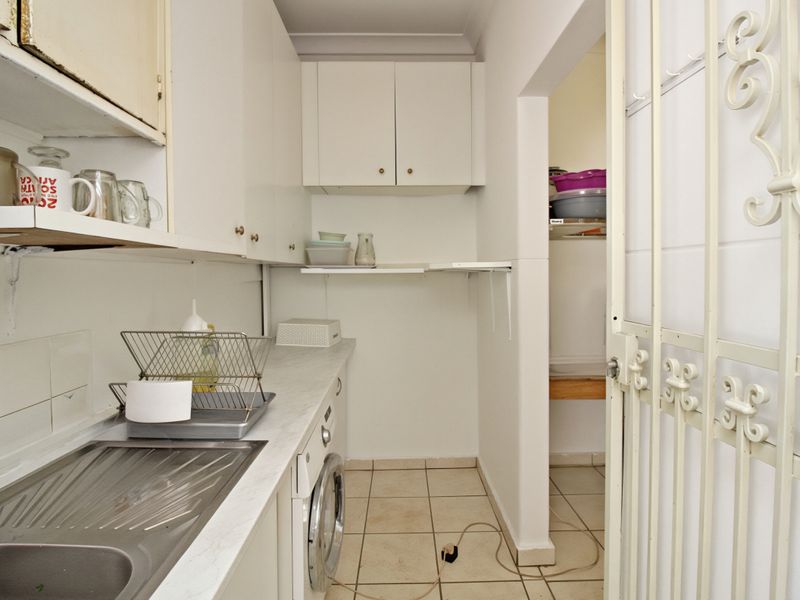 A functional laundry area featuring built-in cabinetry, a stainless steel sink, and tiled flooring, with an adjacent utility space accessible via a security gate.