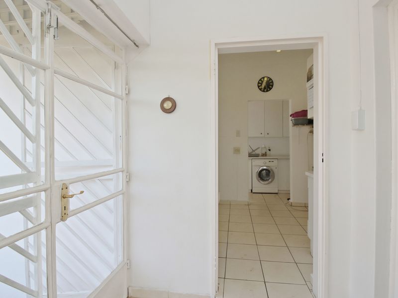 A functional laundry area featuring tiled flooring, built-in cabinetry, and a sink, accessible through a secure metal gate.