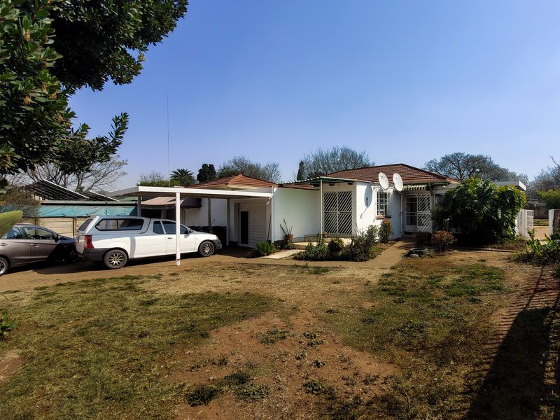 Front view of a single-story house featuring a paved driveway, carport, and established garden area.