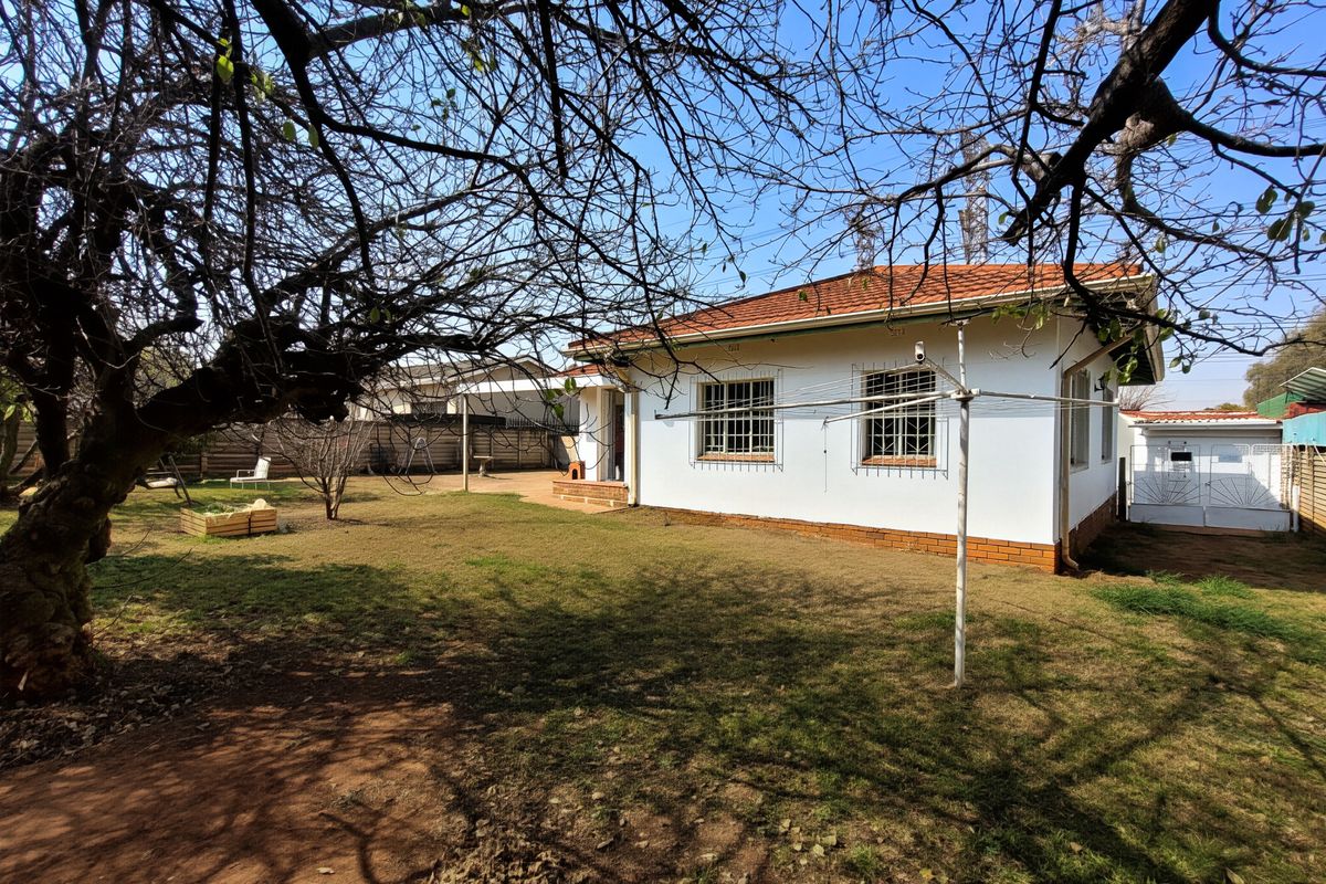 Rear view of the house featuring a white facade, terracotta tiled roof, security bars on windows, and a spacious garden area.
