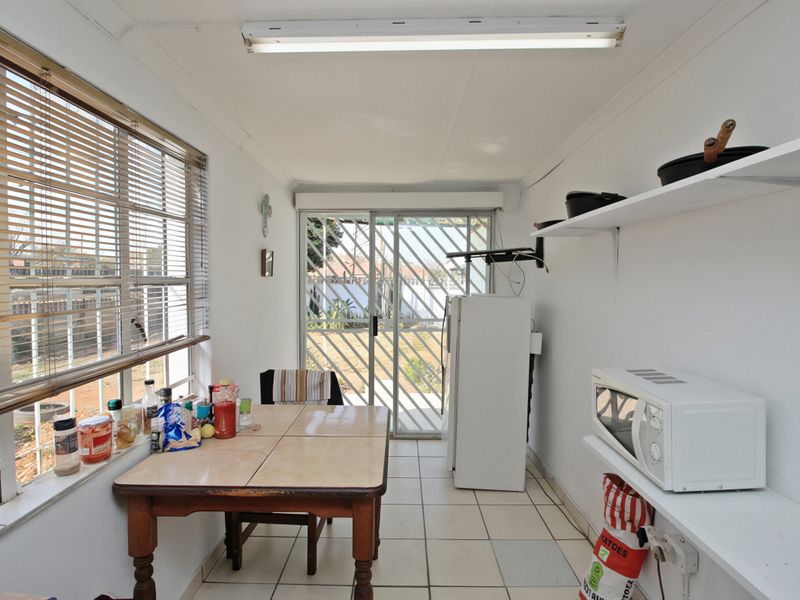 A functional scullery or utility area featuring tiled flooring, built-in shelving, and direct access to the rear garden via a sliding glass door.