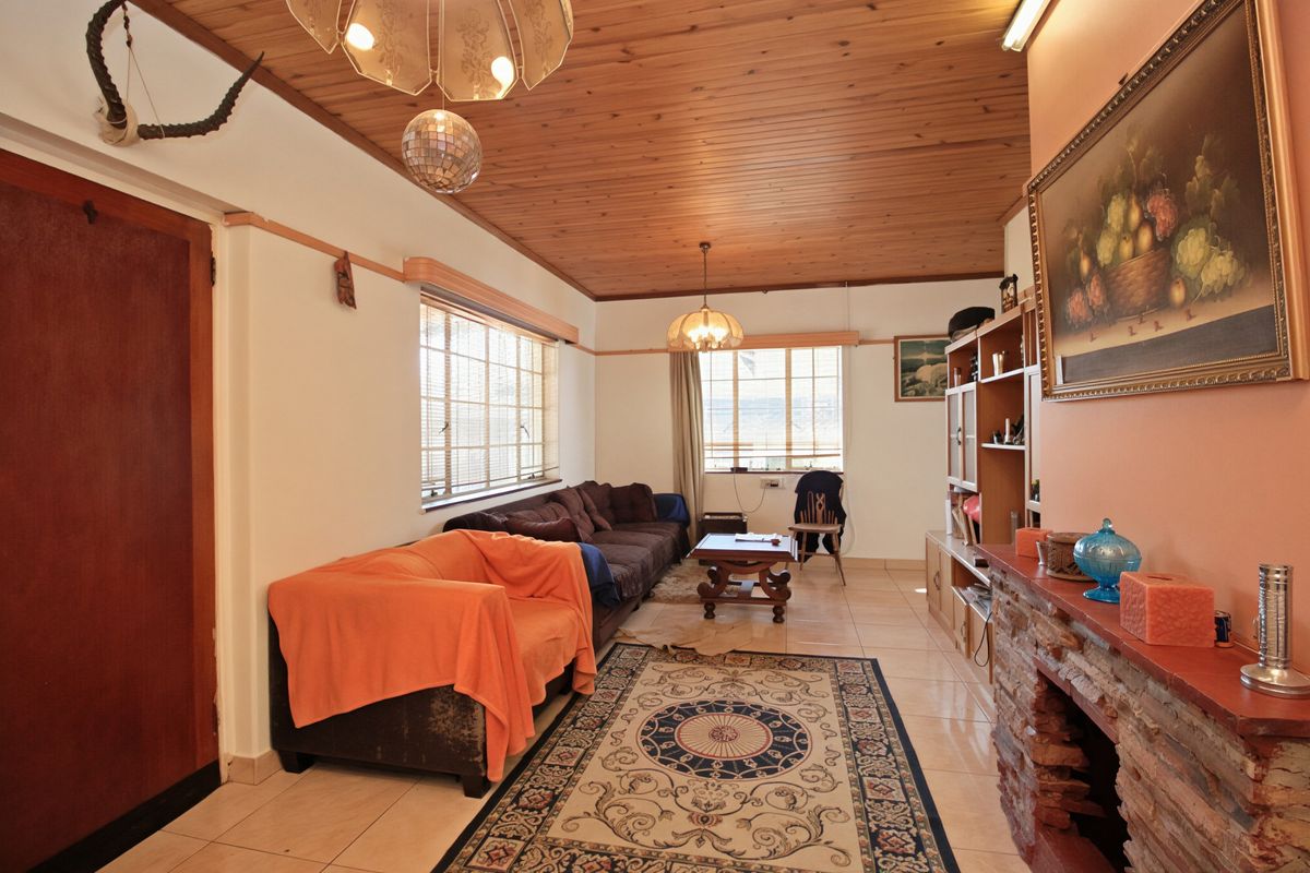 A living room featuring a timber-clad ceiling, tiled flooring, and a rustic stone fireplace, offering a dated but functional living space.