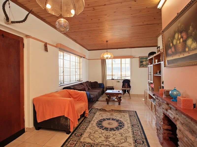 A living room featuring a timber-clad ceiling, tiled flooring, and a rustic stone fireplace, offering a dated but functional living space.