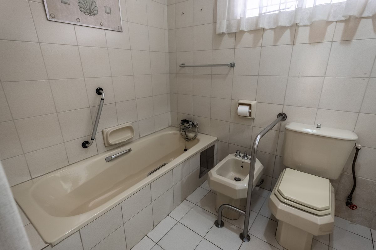 A functional bathroom featuring a bathtub, bidet, and toilet, equipped with safety grab rails and finished with neutral wall and floor tiling.
