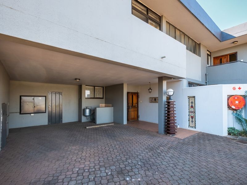 Covered carport area with paved driveway, featuring a fire safety installation and secure entrance access to the retirement village unit.