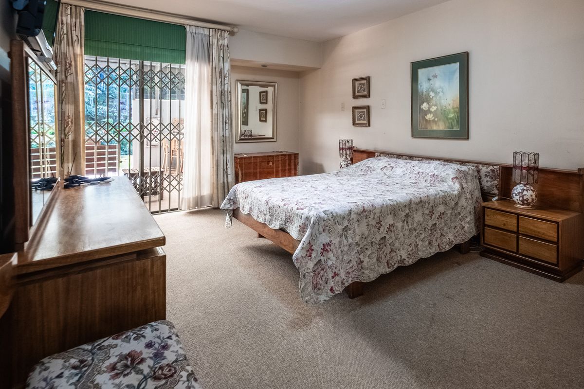 A spacious bedroom featuring built-in wooden headboard and bedside cabinetry, carpeted flooring, and a sliding glass door providing access to an outdoor patio area.