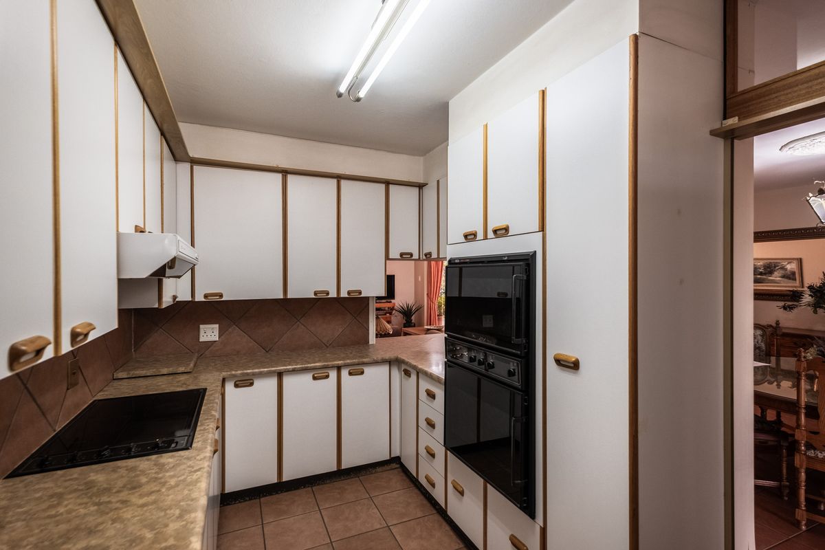 A functional kitchen featuring white cabinetry with wood trim, laminate countertops, tiled backsplash, and built-in oven and cooktop appliances.