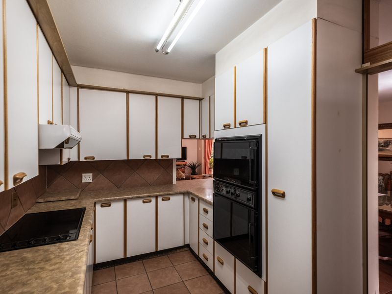 A functional kitchen featuring white cabinetry with wood trim, laminate countertops, tiled backsplash, and built-in oven and cooktop appliances.