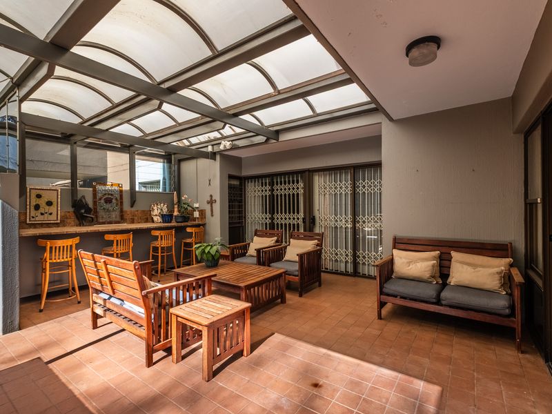 A covered patio area featuring a built-in bar counter, tiled flooring, and a translucent roof, providing a functional outdoor entertainment space.