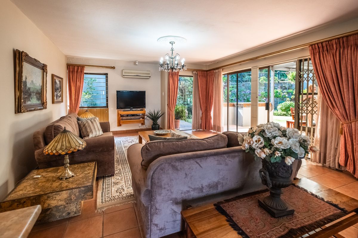 Spacious living room featuring tiled flooring, a ceiling chandelier, and large sliding glass doors providing direct access to the outdoor patio and garden area.