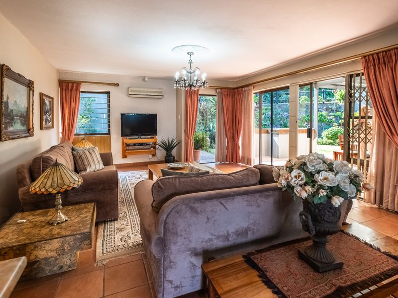 Spacious living room featuring tiled flooring, a ceiling chandelier, and large sliding glass doors providing direct access to the outdoor patio and garden area.