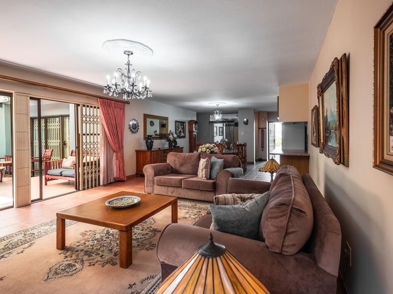 Spacious open-plan living area featuring tiled floors, decorative ceiling roses with chandeliers, and large sliding doors providing access to the patio.