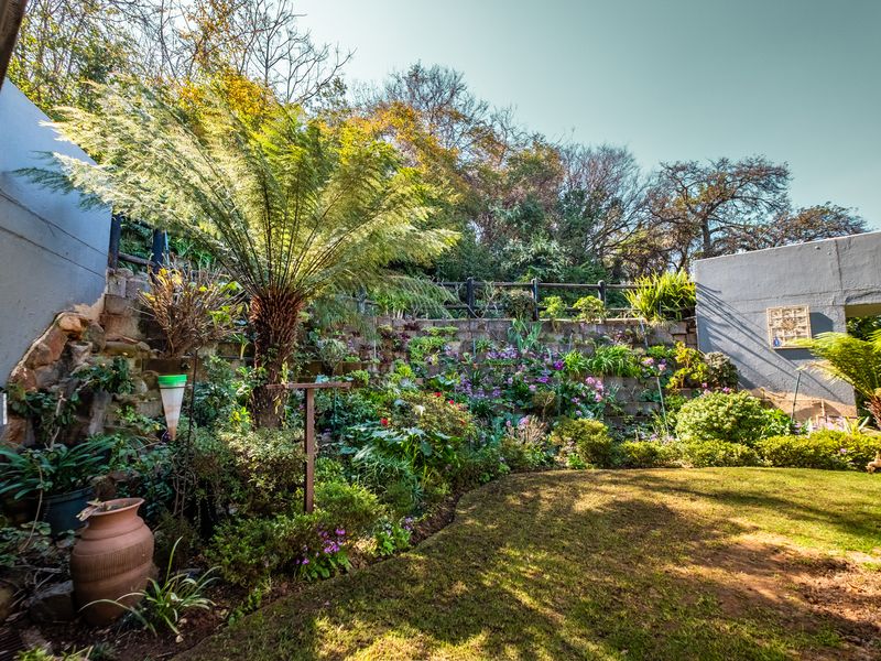 A well-maintained terraced garden featuring established plantings, a lush lawn, and stone retaining walls within a retirement village setting.