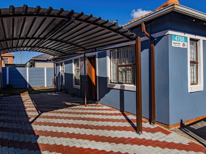 Front exterior view of the property featuring a paved driveway, a covered carport, and blue painted walls with security bars on the windows.