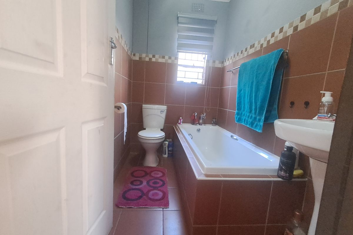 A functional bathroom featuring a built-in bathtub, pedestal basin, and toilet with tiled finishes throughout.