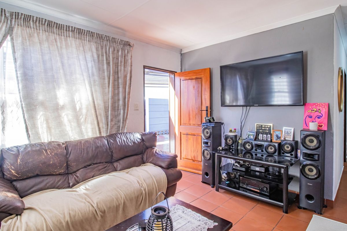 A living room featuring tiled flooring, a wooden door leading to the exterior, and a wall-mounted television setup.