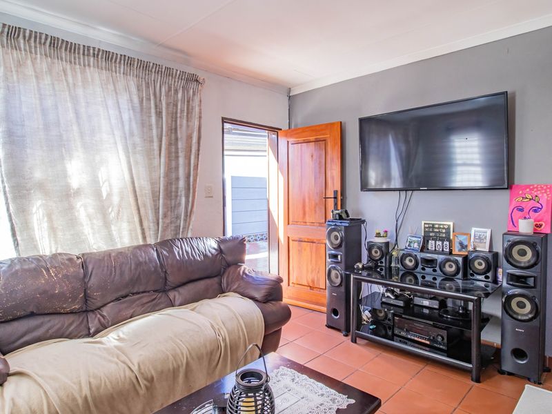 A living room featuring tiled flooring, a wooden door leading to the exterior, and a wall-mounted television setup.