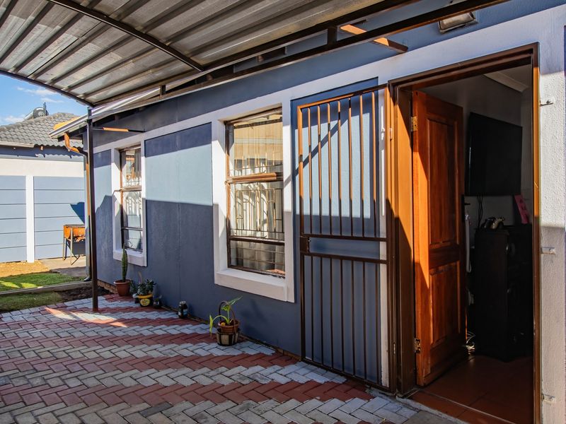 A covered patio area featuring paved flooring, a corrugated metal roof, and a secure entrance gate leading into the home.
