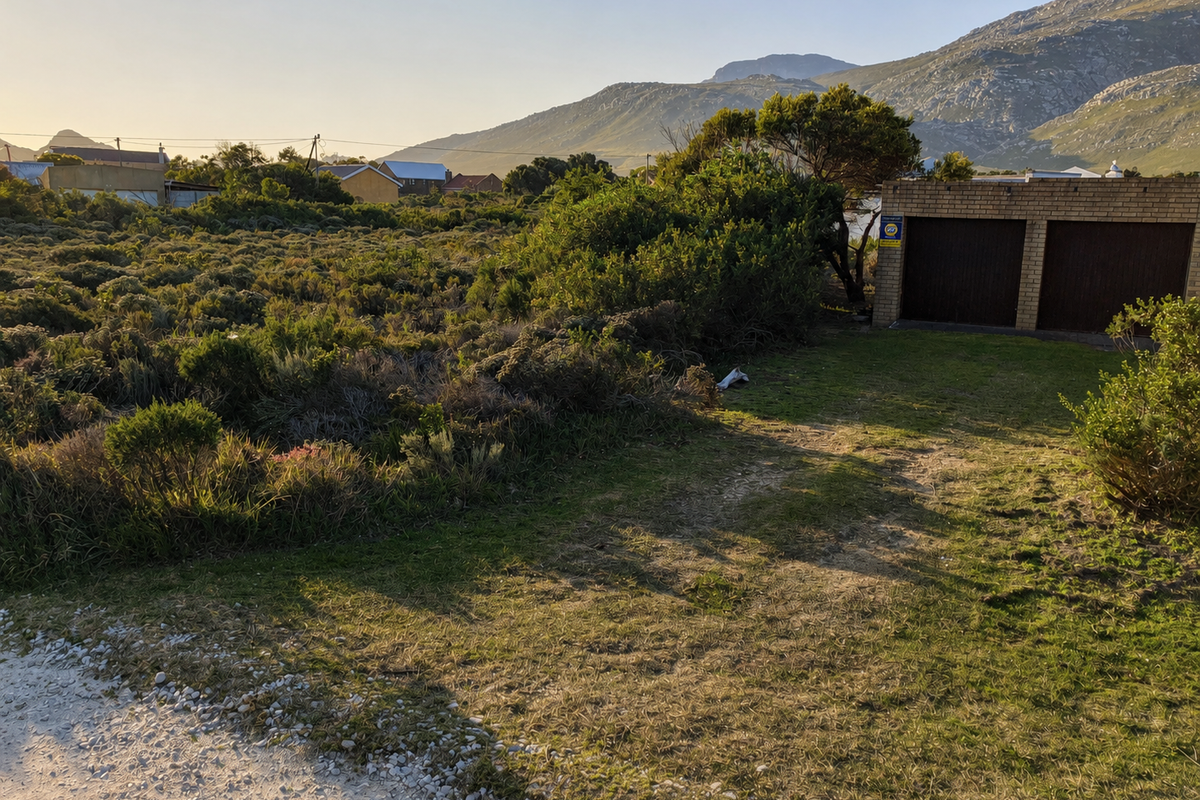A view of a vacant residential plot featuring native vegetation and an existing double garage structure with mountain views in the background.