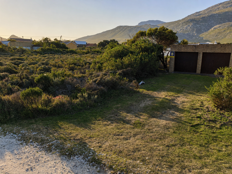 A view of a vacant residential plot featuring native vegetation and an existing double garage structure with mountain views in the background.