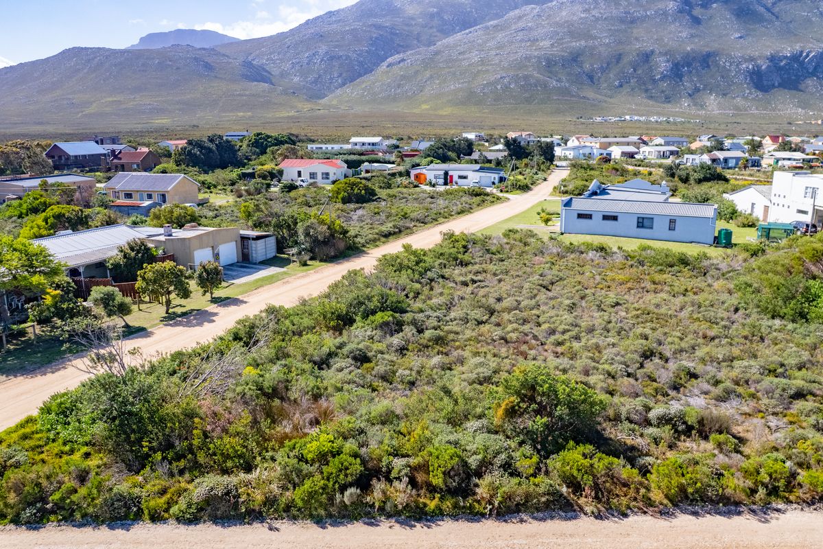 Aerial view of a vacant residential plot featuring native vegetation and direct access to a dirt road in a scenic coastal neighborhood.
