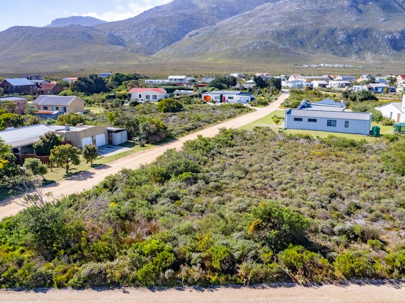 Aerial view of a vacant residential plot featuring native vegetation and direct access to a dirt road in a scenic coastal neighborhood.