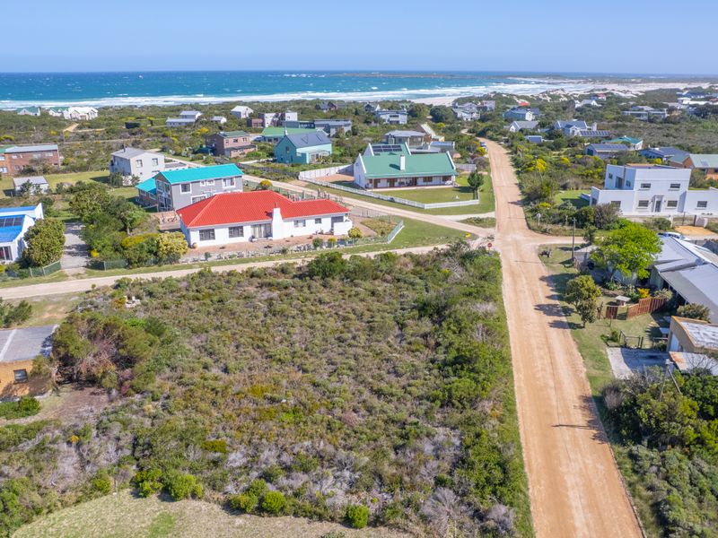 An aerial view of a vacant residential plot situated in a coastal neighborhood with direct access to a dirt road.