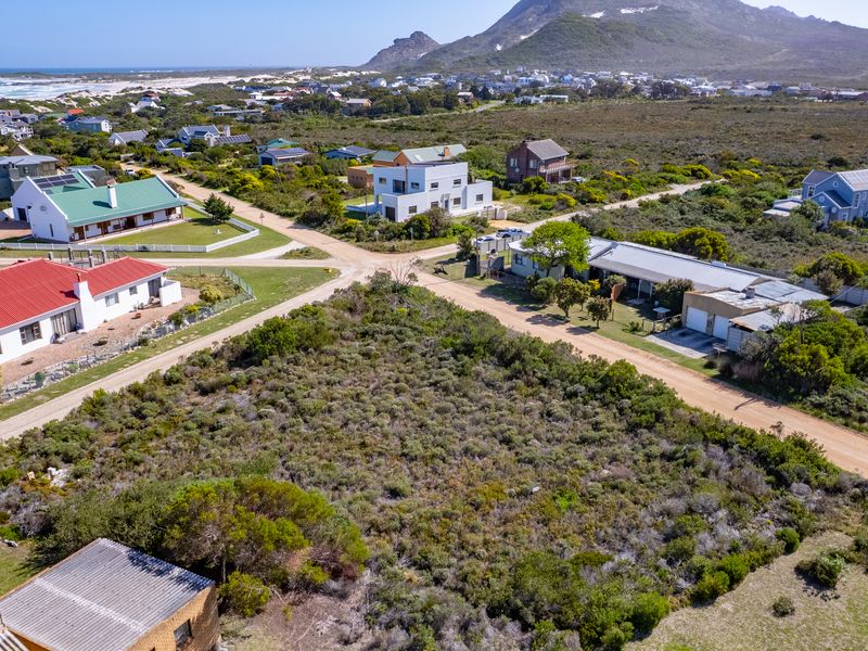 Aerial view of a vacant residential plot situated in a coastal neighborhood with surrounding homes and natural vegetation.