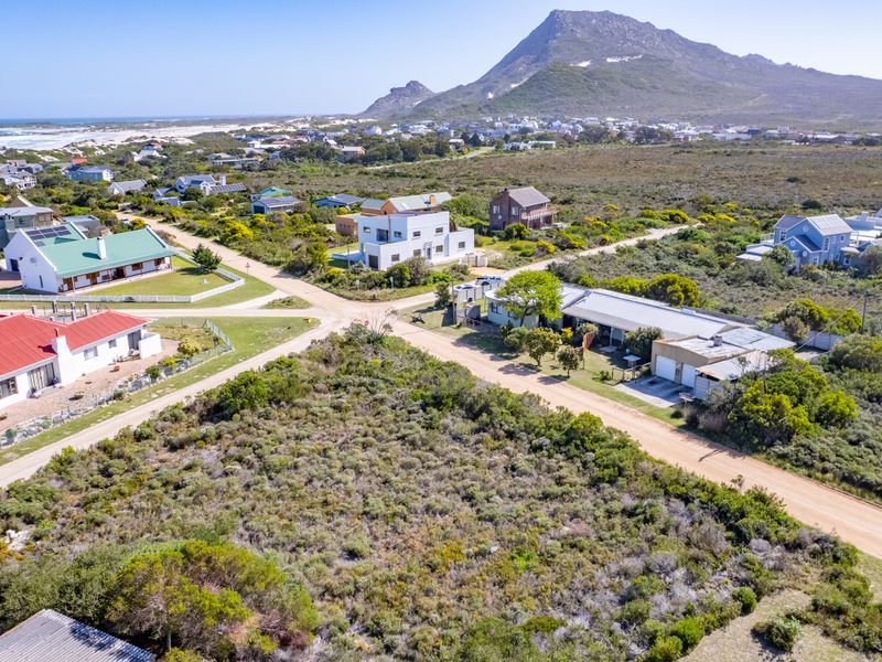 An aerial view of a vacant residential plot situated in a coastal neighborhood with surrounding homes and natural landscape.