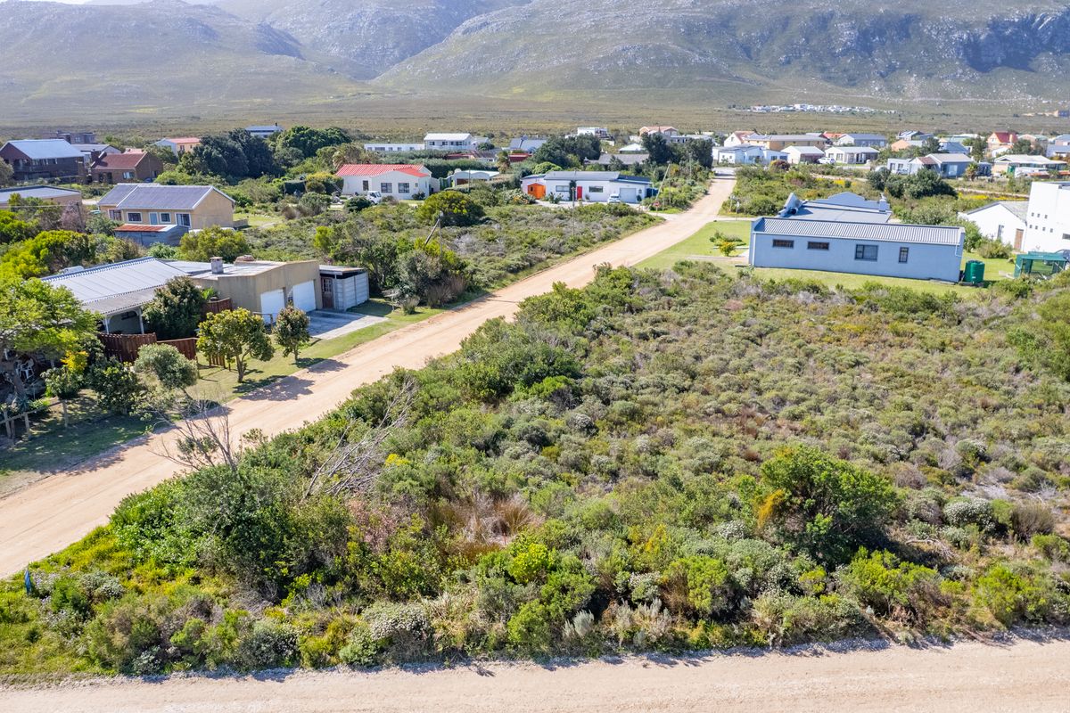 Aerial view of a vacant residential plot featuring native vegetation and direct access to a dirt road in a coastal neighborhood.