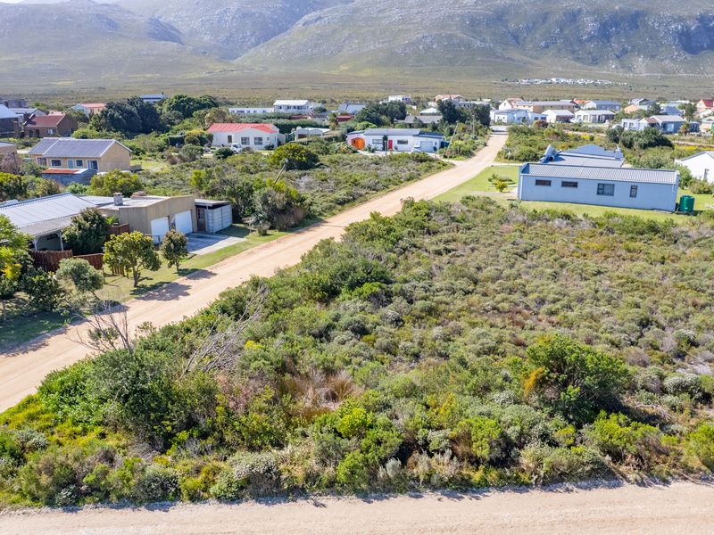 Aerial view of a vacant residential plot featuring native vegetation and direct access to a dirt road in a coastal neighborhood.