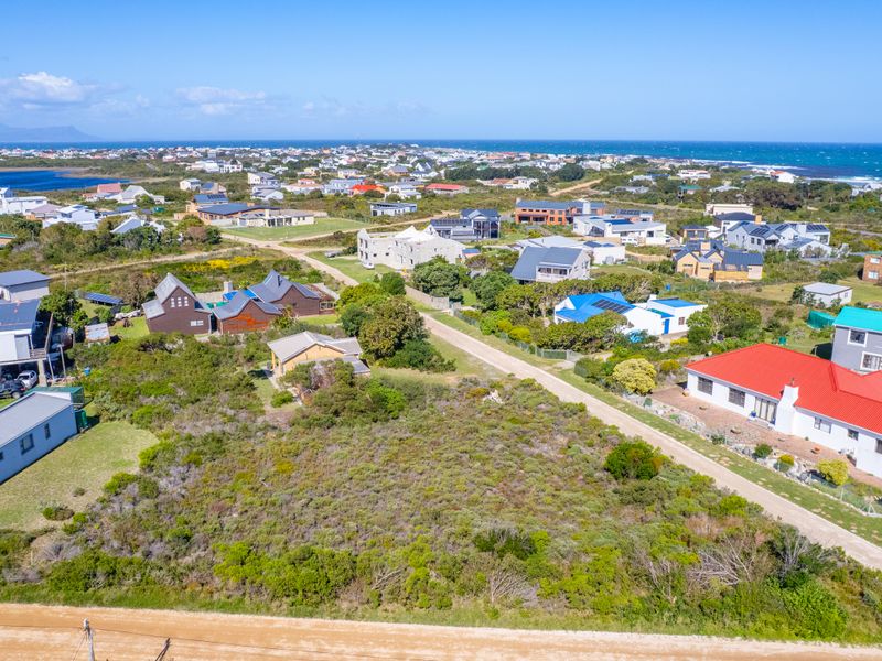An aerial view of a vacant residential plot situated in a coastal neighborhood, surrounded by established homes and natural vegetation.