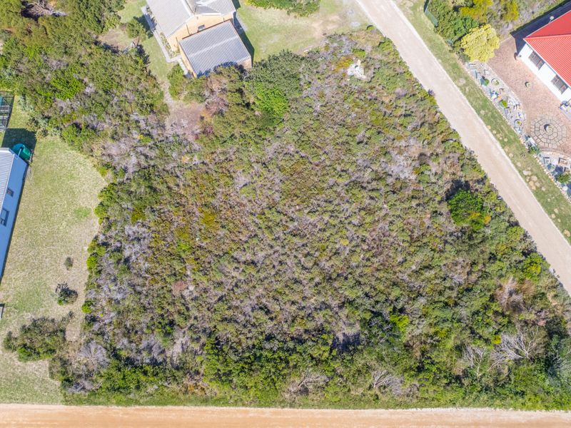 An aerial view of a vacant residential plot covered in native vegetation, situated in a developed neighborhood with adjacent properties.