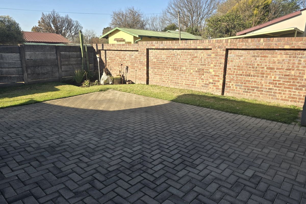 A private rear garden featuring a paved patio area, a well-maintained lawn, and secure brick and precast concrete boundary walls.