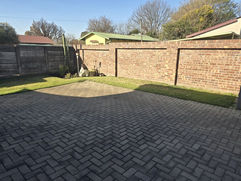 A private rear garden featuring a paved patio area, a well-maintained lawn, and secure brick and precast concrete boundary walls.