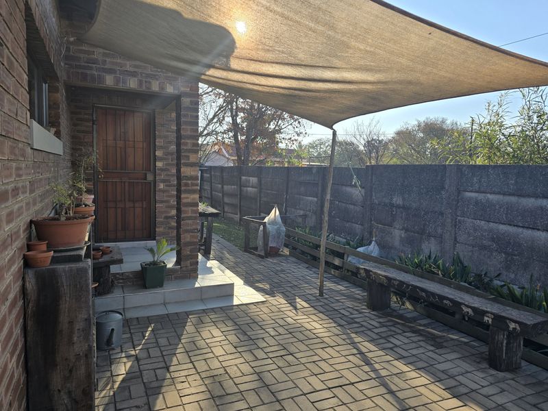 Outdoor patio area featuring brick paving, a shade sail for sun protection, and a private enclosed garden space with a boundary wall.